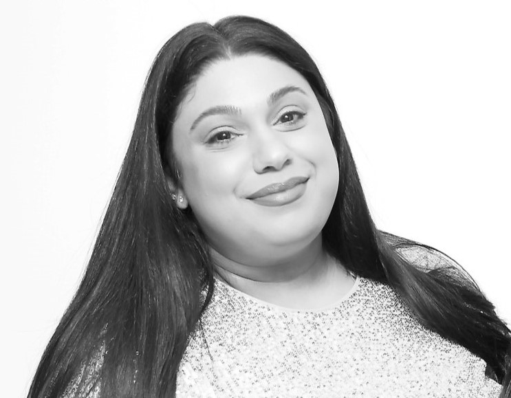 This is a grey scale image of me. My black hair is middle parted, falling down on my shoulders. I am wearing a glitter dress. I am smiling and looking towards the camera. 